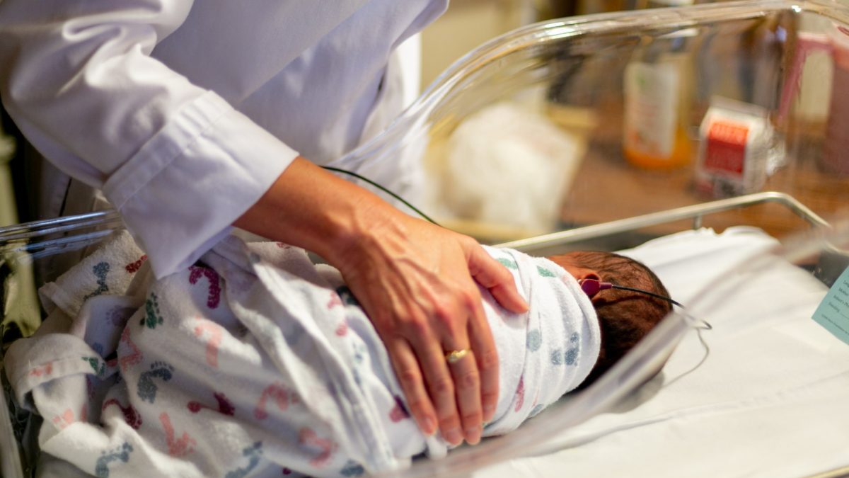 Obstetrician comforting baby in cradle