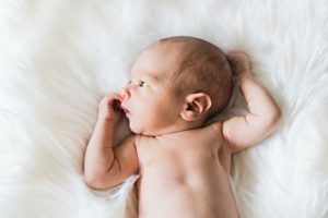 Curious newborn baby laying on a soft, gray blanket