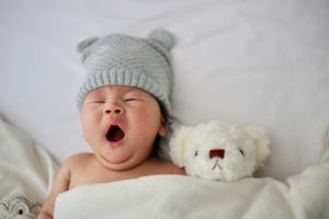 newborn baby yawning while laying next to teddy bear in hospital