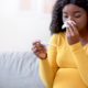 Woman in yellow checking temperature before using pregnancy safe cold medicine